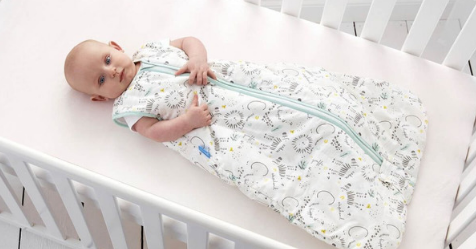 Baby laying in cot while wearing sleeping bag suit
