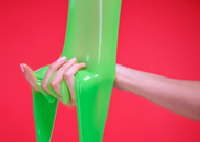Hand held out against red background as green slime is poured onto it.