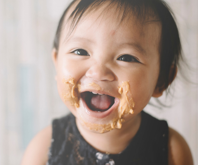 Close up of laughing, brown eyed baby with a very happy face which is smeared with peanut butter.